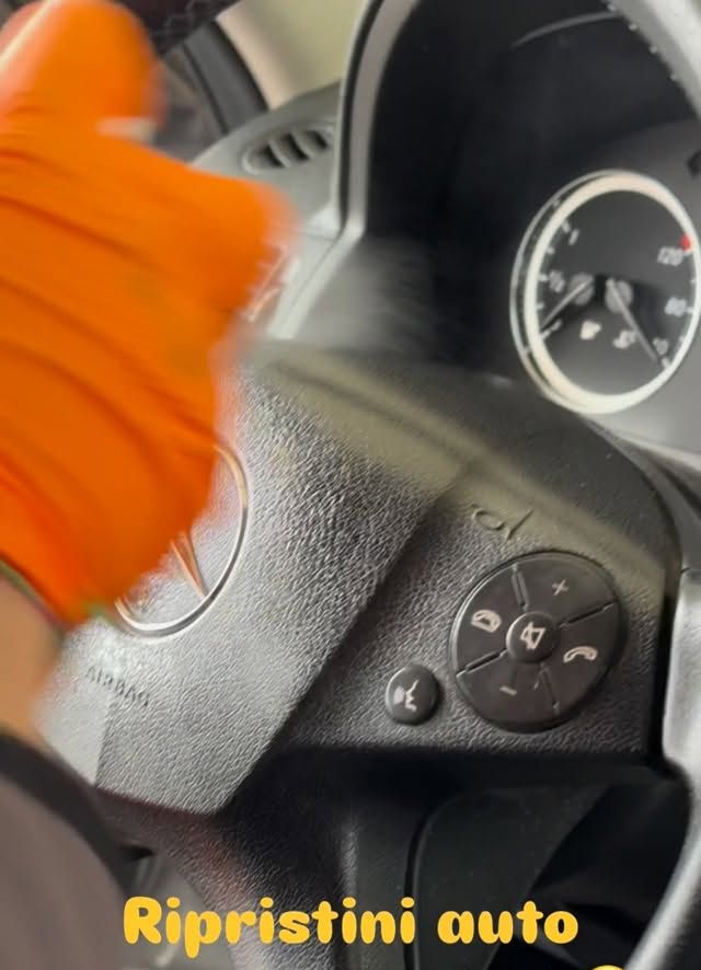 Una mano con il guanto arancione che pulisce il volante